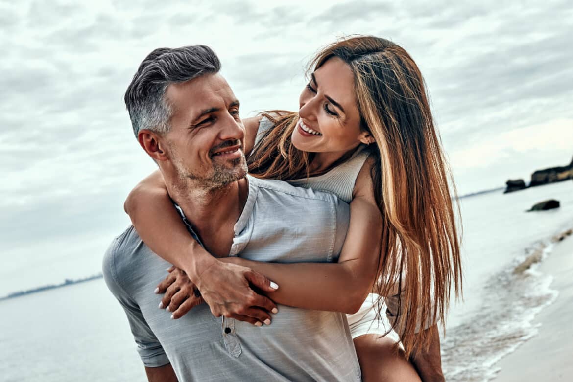 Smiling man giving woman a piggy back at the beach.