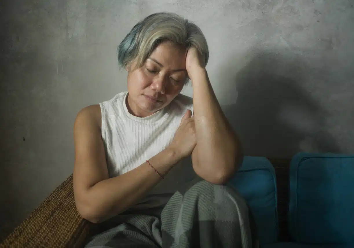 Mature woman on living room couch feeling depressed and scared suffering from menopause symptoms.