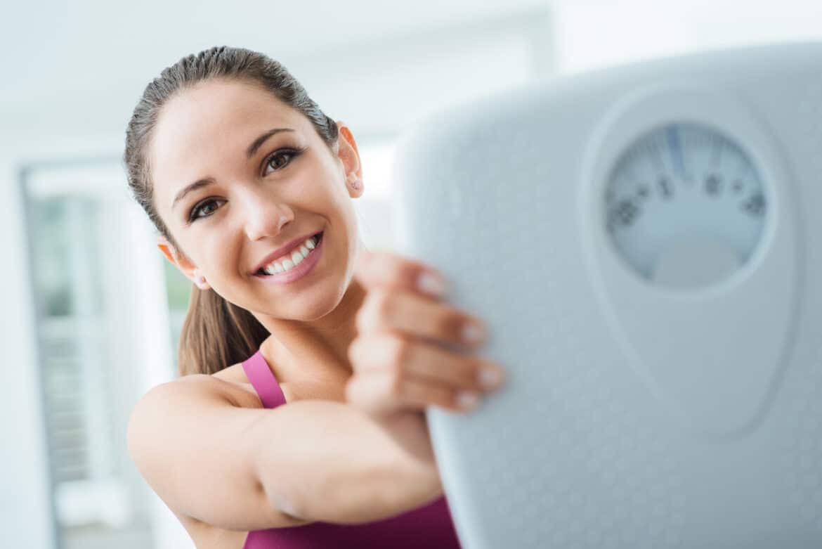 Happy woman losing weight and showing a scale, dieting and fitness.